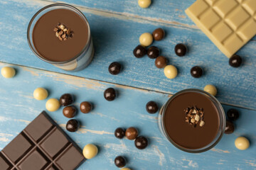 Top view of Two Chocolate dessert in glass (yogurt or cream, cookies )with chocolate balls (black chocolate, milk chocolate and white chocolate ). Sweet dessert concept on blue wooden background