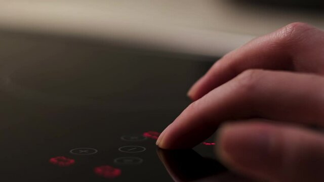 Close up of a modern induction stove control panel, household utensils. Concept. Female hand touching sensor panel to turn it on, modern technologies for the kitchen. 