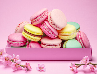 Colorful sweet macarons or macaroons, flavored cookies in the paper box on pink background.