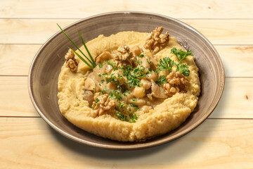 Hummus with parsley, olive oil and walnuts. Israeli chickpea cream in earthenware bowl on wooden table