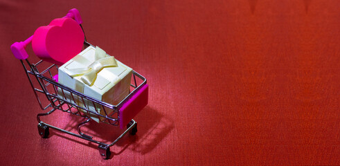 Shopping cart with pink heart and gift box on red background. Valentines day shopping. Place for...