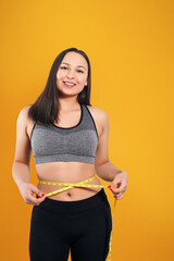 A slender woman measures her waist with a measuring tape. n a yellow background.