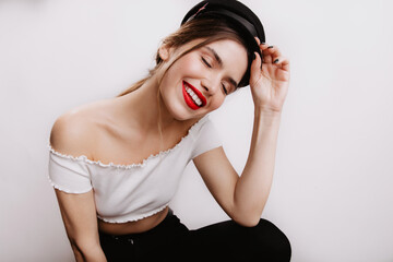 Fototapeta premium Close-up portrait of lady in cap and short top.Woman with red lipstick smiling sitting on white background