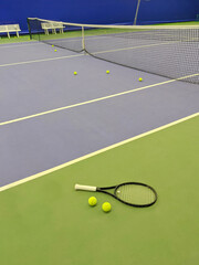 Close up view of tennis racket and two balls on the green clay tennis court