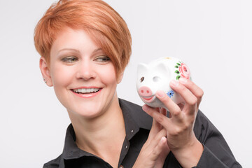 happy red haired woman looks happily at her piggy bank
