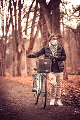 Fototapeta na wymiar Person walking with a bike and a face mask on in the autumn on a small road in a park