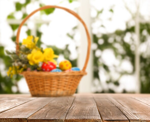 Empty wooden surface and wicker basket with colorful Easter eggs on background