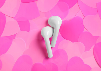 Modern earphones on pile of pink hearts, flat lay. Listening love music songs