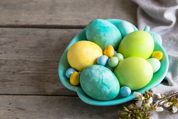colorful easter eggs in a turquoise plate on a shabby wooden background