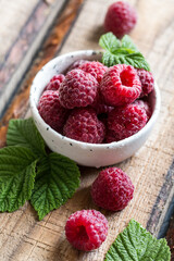 fresh juicy raspberries with green leaves in a plate on a wooden table. Healthy berry, organic food, antioxidant