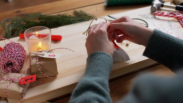winter holidays and hobby concept - hands with bag and rope making advent calender or packing christmas gift at home