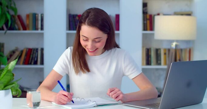 Young woman studying online chatting to web camera video call on coronavirus lockdown. Happy student girl sitting at pc table talking to teacher making notes slow motion. Distant learning education 