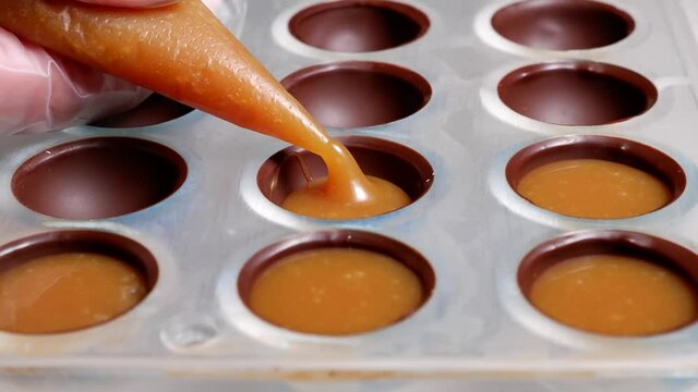 pouring the filling into the form of chocolates from a pastry bag