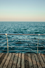 Old wooden rustic pier with metal handrail. Blue cold sea view skyline. Winter seascape. Central composition. Concept of enjoying nature, nobody, loneliness, freedom, tranquility, dreaming, thinking