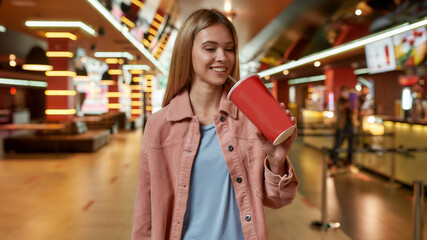 Portrait of lovely young woman smiling, drinking soda, posing in front of a concession stand in a movie theater