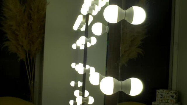 Beautiful mirror with bright white lamps in the beauty salon. Make-up or barber mirror. Square mirror with bulbs in dressing room. Interior of the dressing room or beauty salon with modern lighting. 
