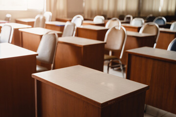 Many wooden tables and chairs well arranged in the university classroom but no student. Empty classroom with no student due to school being lockdown during COVID-19 pandemic.