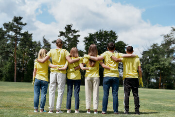 Great teamwork. Group of young volunteers wearing uniform and rubber gloves hugging and looking at...