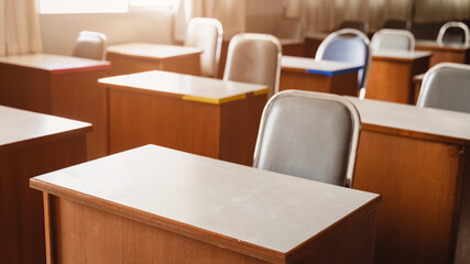 Fototapeta premium Many wooden tables and chairs well arranged in the university classroom but no student. Empty classroom with no student due to school being lockdown during COVID-19 pandemic.