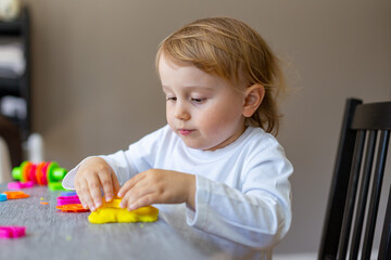 Cute little boy moulds from colored plasticine on table. Home schooling. Creative leisure with children during corona virus quarantine staying at home.