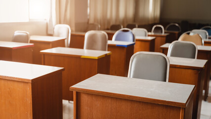 Many wooden tables and chairs well arranged in the university classroom but no student. Empty classroom with no student due to school being lockdown during COVID-19 pandemic.