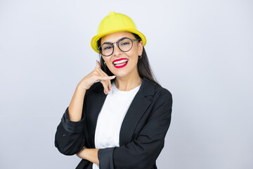 Young architect woman wearing hardhat smiling doing phone gesture with hand and fingers like talking on the telephone