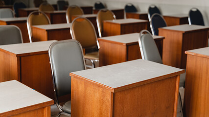 Many wooden tables and chairs well arranged in the university classroom but no student. Empty classroom with no student due to school being lockdown during COVID-19 pandemic.