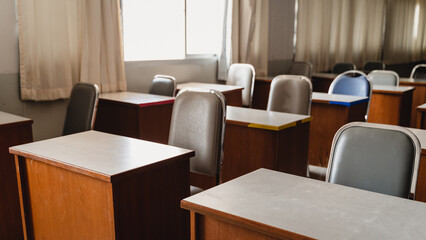 Many wooden tables and chairs well arranged in the university classroom but no student. Empty classroom with no student due to school being lockdown during COVID-19 pandemic.