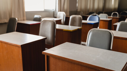 Many wooden tables and chairs well arranged in the university classroom but no student. Empty classroom with no student due to school being lockdown during COVID-19 pandemic.