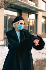 Fototapeta na wymiar senior stylish woman in beret and elegant black coat and in medical mask walking outdoor and counting time till the end of pandemic. Lockdown, pandemic, protection concept 