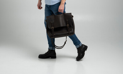Brown men's shoulder leather bag for a documents and laptop holds by man in a blue shirt and jeans...