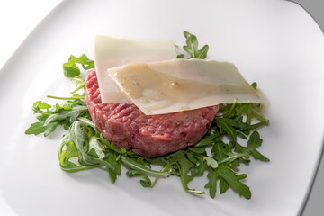 fresh beef tartare, raw minced meat from piedmontese Fassona breed cattle.with cheese flakes, on rocket leaves in white plate