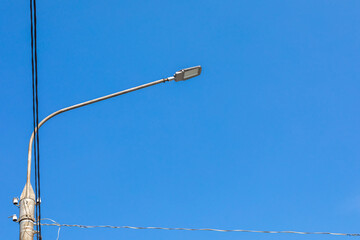 concrete electric pole with a street lamp and a wires against a blue sky