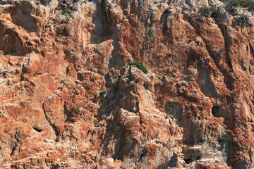 Rote Felsküste an der Ostküste Mallorcas mit leichtem Bewuchs.