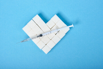heart made of sugar cubes and insulin syringe on blue background place copy diabetes concept