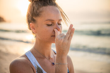 Woman's face close up. Yogi woman practicing Nadi Shodhana Pranayama, Alternate Nostril Breathing. Breathing exercise. Self care concept. Sunset time. Yoga retreat. Thomas beach, Bali