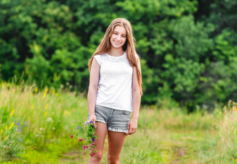 Obraz premium Smiling girl with field flowers bouquet