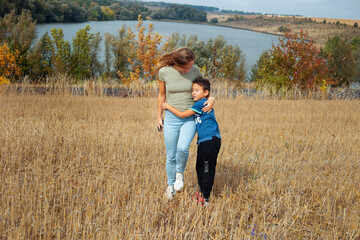 Mother and son are playing together outdoors in warm autumn day  - 407665401