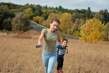 Mother and son are playing together outdoors in warm autumn day  - 407665451