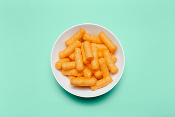 Top view of white bowl with corn puffs on green background.