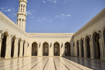 An inner courtyard surrounded by walls with arches in Sultan Qaboos Grand Mosque. The sky is blue. Muscat, Oman.