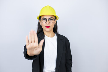 Young architect woman wearing hardhat serious and doing stop sing with palm of the hand.