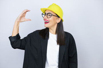 Young architect woman wearing hardhat smiling and confident gesturing with hand doing small size sign with fingers . Measure concept