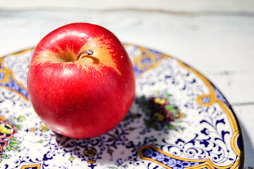 ripe red apple on beautiful ornamental plate on a wooden table 