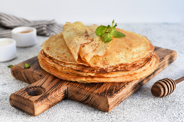 A stack of thin pancakes with sour cream and honey on a wooden board on a concrete background.