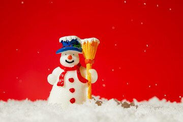 Closeup of a cute snowman toy on fake snow against a red background