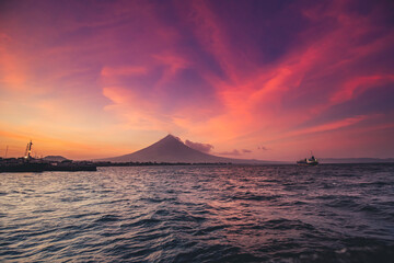Philippine ocean sunrise silhouette, Volcano Mayon erupt cloud haze. Tropic Asia seascape of water transport: ships, boats at harbor. Picturesque sea bay and coast with small cottage, lodge, building