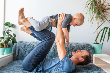 Happy baby boy flying in father's arms lookingdad holding lifting cute little child son playing plane on couch