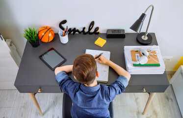 Top view of unrecognizable boy doing homework on desk in his bedroom