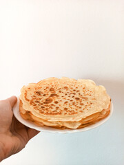 Close up stack of pancakes, hand keeping plate with stack of pancakes on white background. Homemade cooking, lockdown